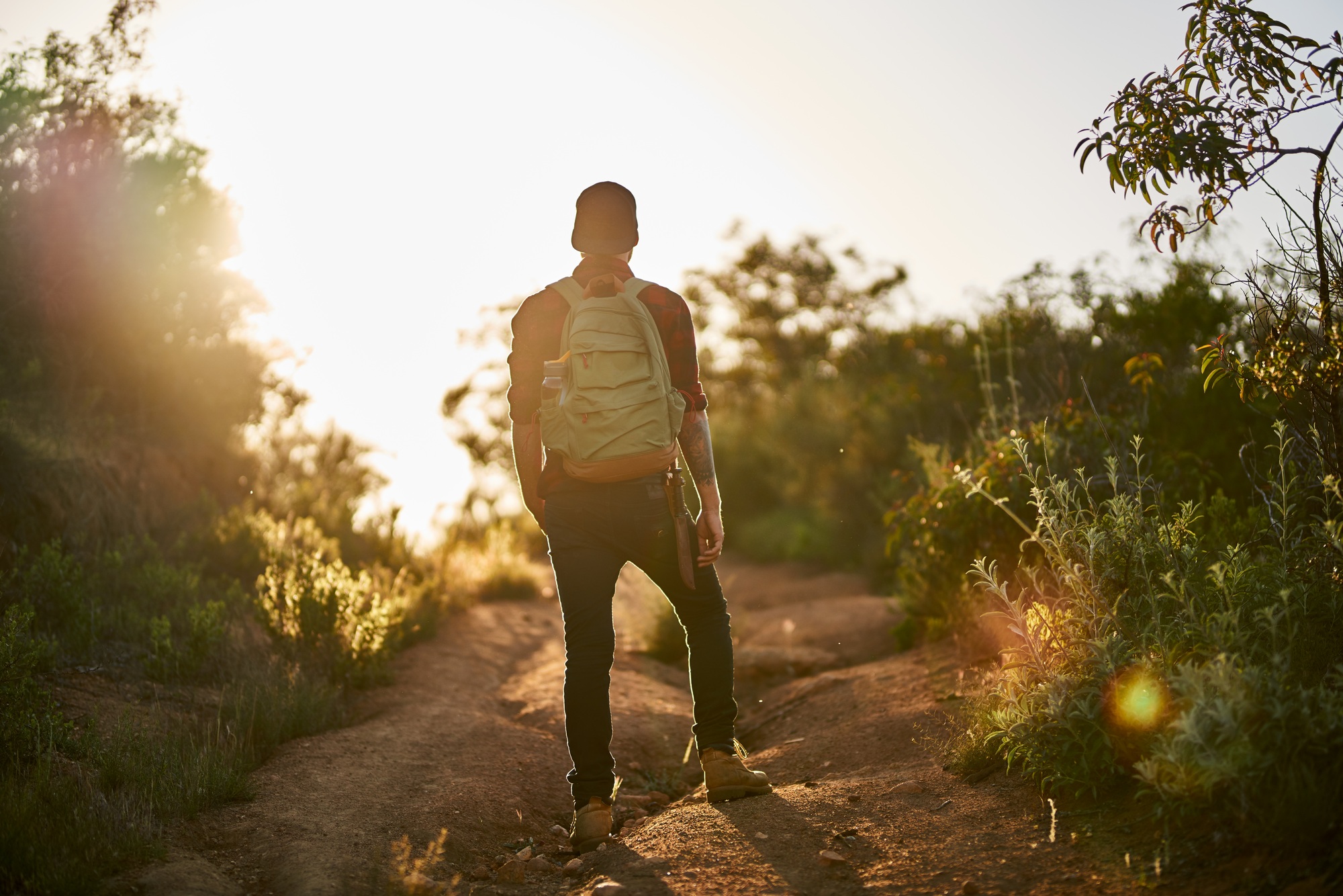 male millennial hiker trekking up trail in southern california during sunset