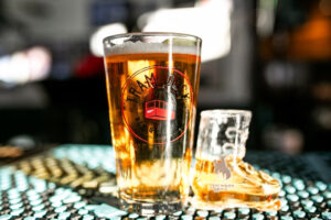 Tall amber beer in a pint glass with a circular tram logo on the front, set on a bar counter.